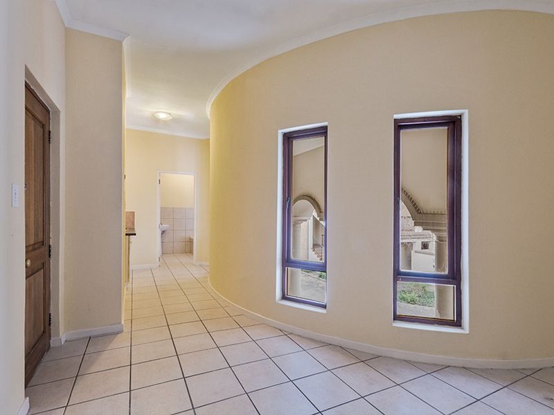 A spacious, curved hallway featuring tiled flooring, timber-framed windows, and neutral wall finishes, providing access to adjacent rooms.