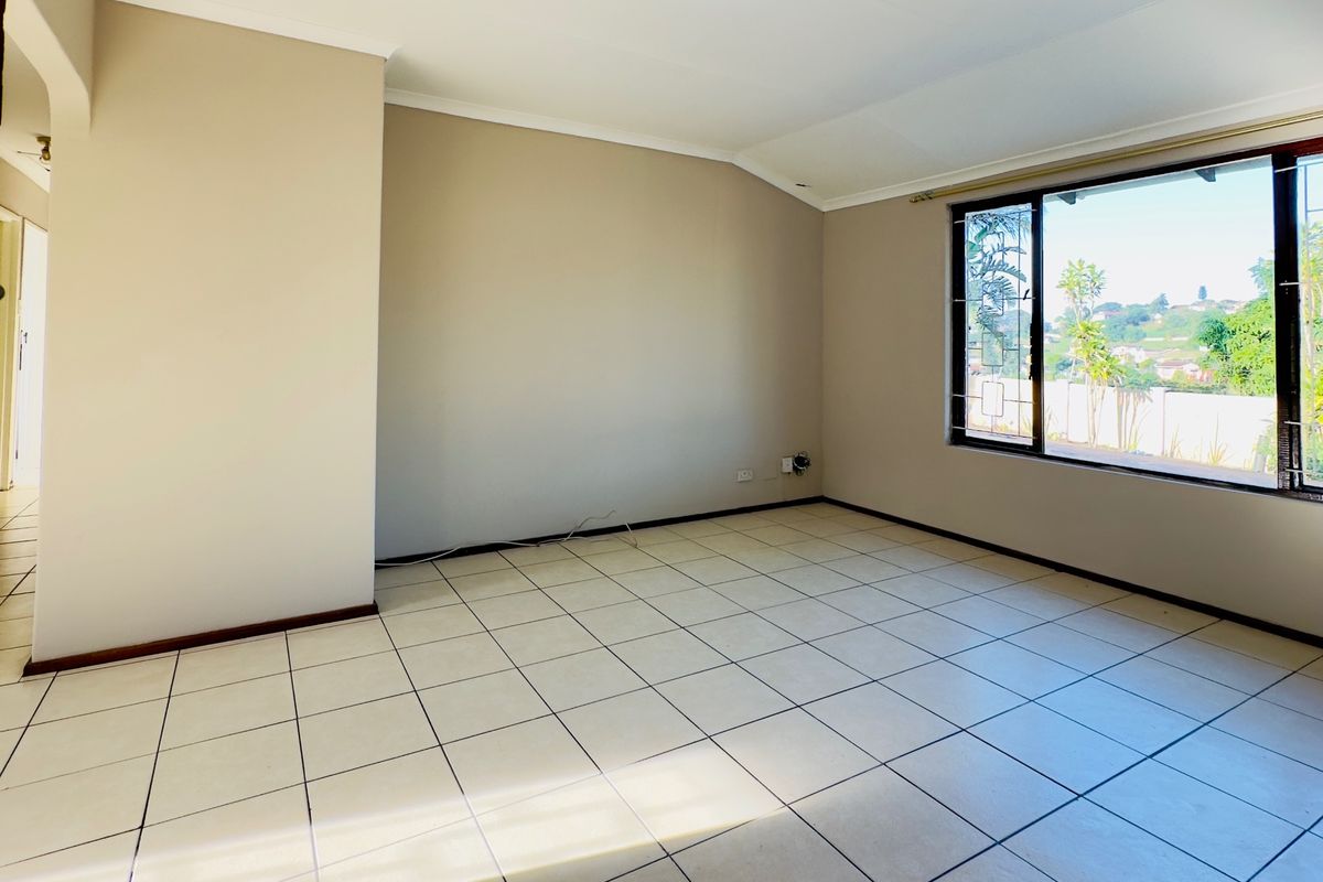 A bright, empty living room featuring neutral wall tones, tiled flooring, and a large window providing natural light and exterior views.