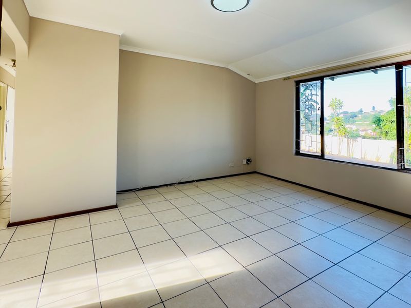A bright, empty living room featuring neutral wall tones, tiled flooring, and a large window providing natural light and exterior views.
