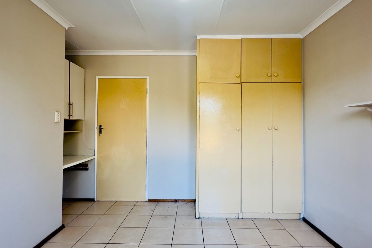 An empty bedroom featuring tiled flooring, built-in cupboards, and a built-in desk area, offering a functional space ready for personalization.