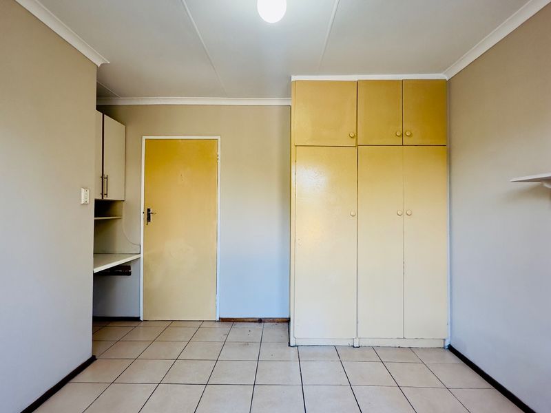 An empty bedroom featuring tiled flooring, built-in cupboards, and a built-in desk area, offering a functional space ready for personalization.
