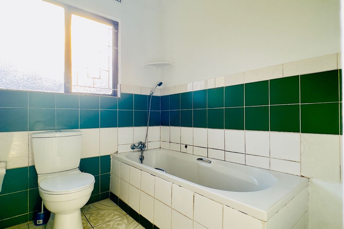 A dated bathroom featuring a bathtub, toilet, and green and white wall tiling. The space requires cosmetic updates to modernize the finishes.