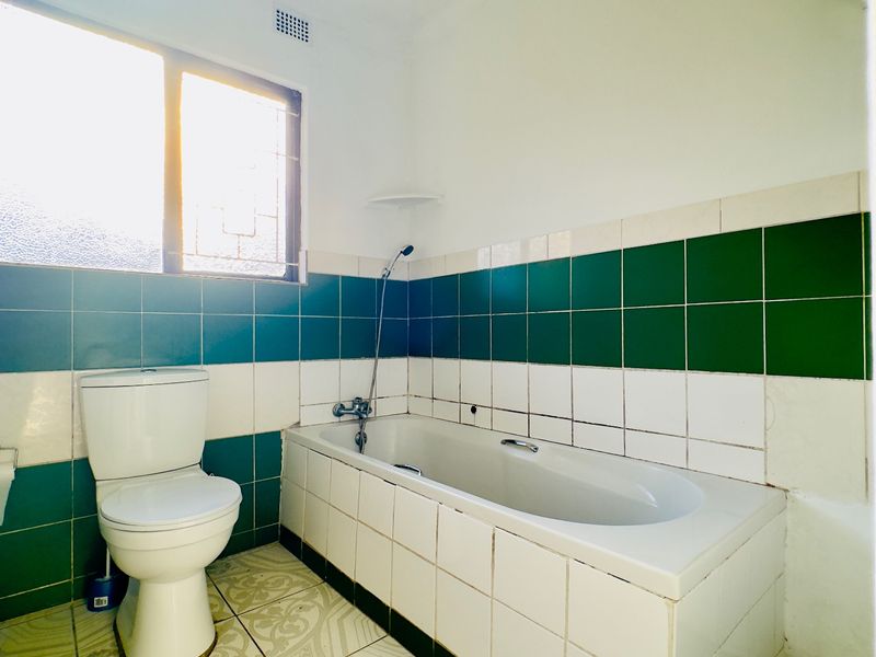 A dated bathroom featuring a bathtub, toilet, and green and white wall tiling. The space requires cosmetic updates to modernize the finishes.