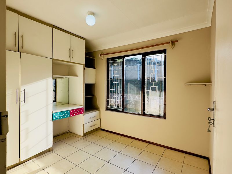 A bedroom featuring built-in cupboards with an integrated vanity, tiled flooring, and security bars on the window.