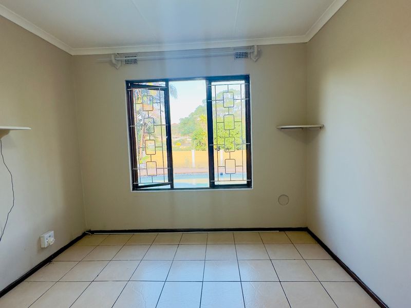A bright, empty bedroom featuring tiled flooring, security bars on the window, and built-in shelving, offering a clean canvas for personalization.