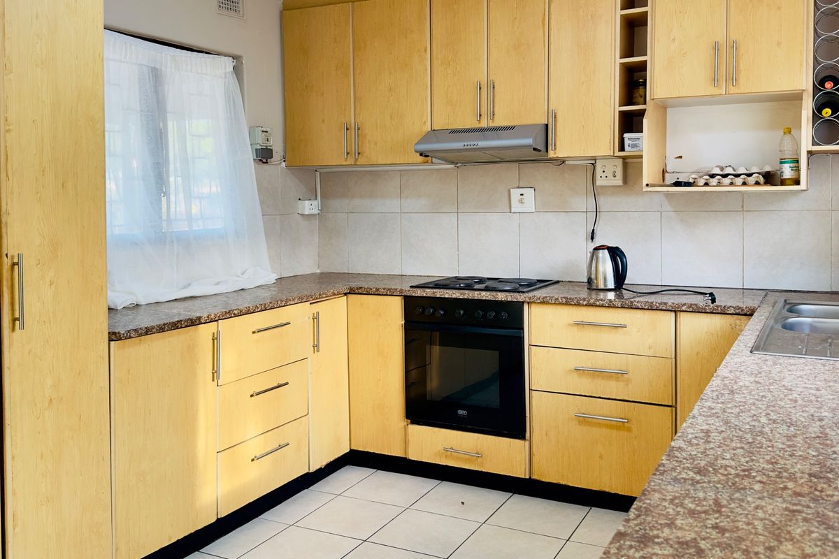 Functional kitchen featuring light wood-look cabinetry, granite-style laminate countertops, built-in oven with hob, and tiled flooring.