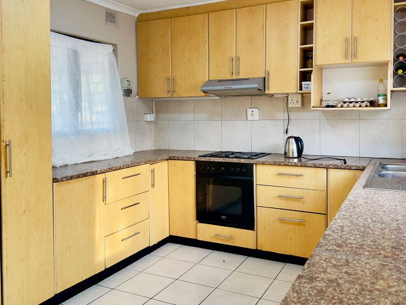 Functional kitchen featuring light wood-look cabinetry, granite-style laminate countertops, built-in oven with hob, and tiled flooring.