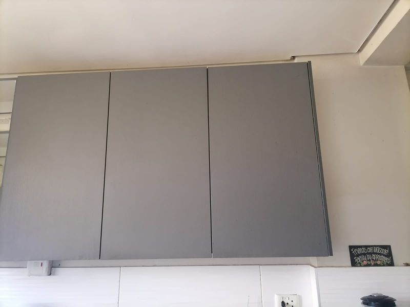 A close-up view of grey wall-mounted kitchen cabinetry featuring a white tiled backsplash and integrated electrical fixtures.