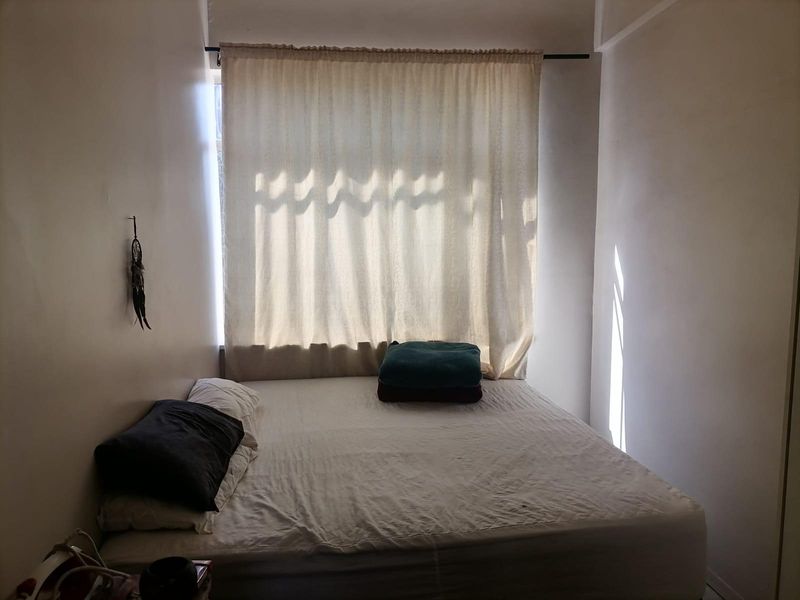 A compact bedroom featuring a large window with a curtain rod, providing natural light to the space.