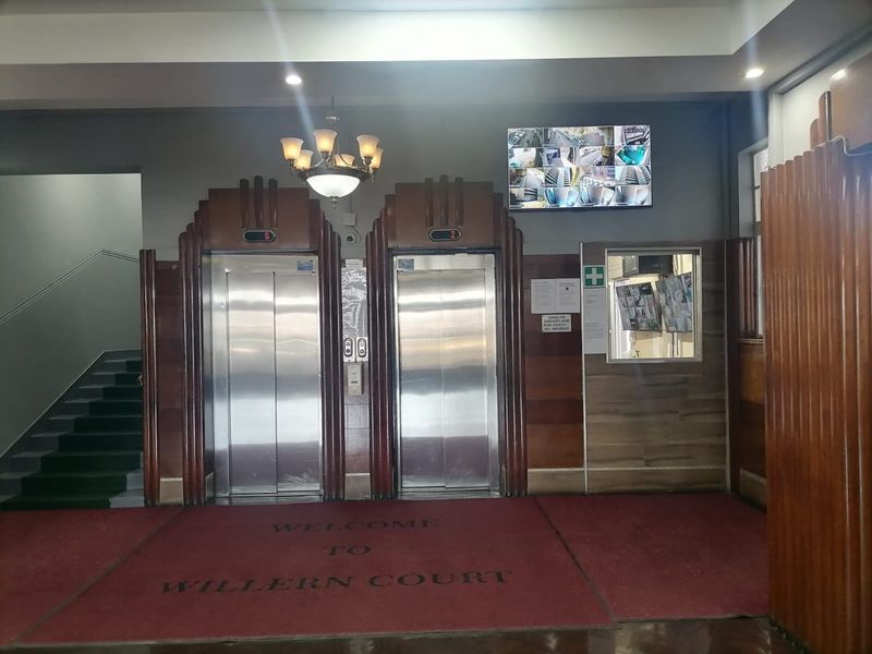 The apartment building entrance lobby features dual elevators, a security monitoring station, and a staircase leading to upper levels.