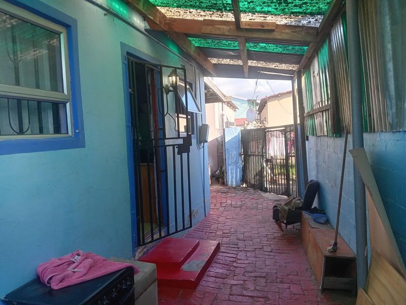 A covered outdoor patio area featuring brick paving, a timber-framed corrugated roof, and a security gate entrance.
