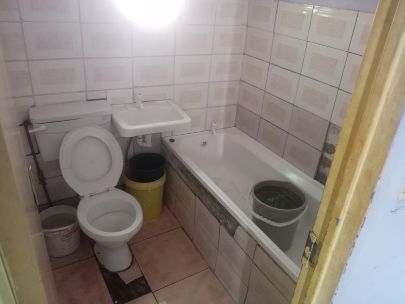 A compact bathroom featuring a toilet, wall-mounted basin, and bathtub, currently requiring maintenance and tile repairs to improve its overall condition.