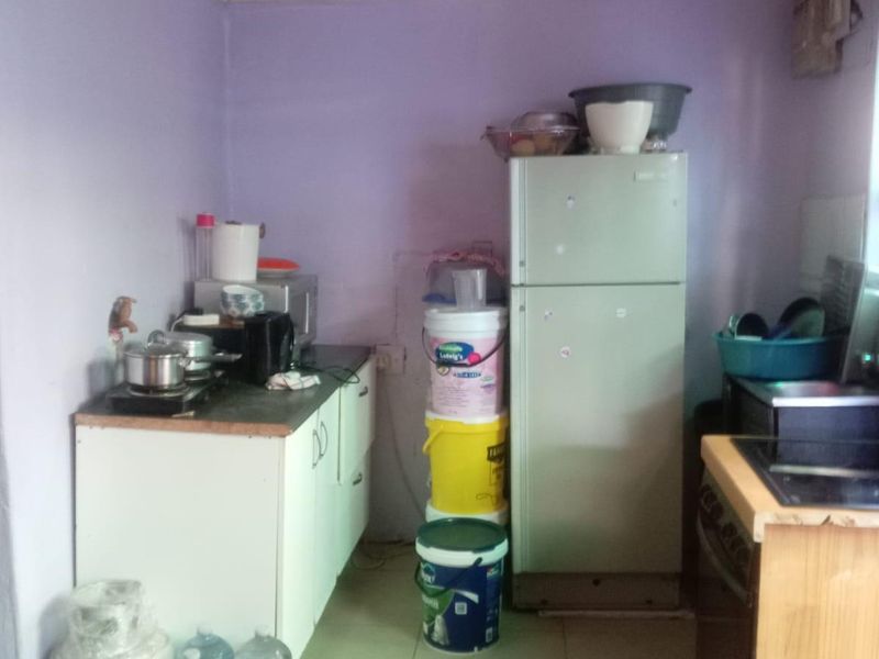 A small, basic kitchen area featuring simple base cabinetry, tiled flooring, and dated wall finishes, requiring significant cosmetic updates and modernization.