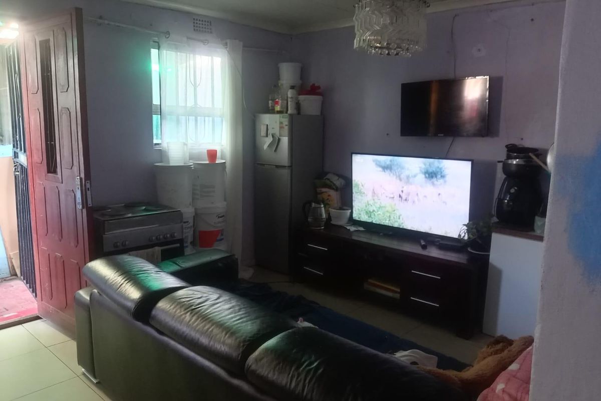 A living room area featuring tiled flooring and a ceiling light fixture, currently showing signs of wear including wall cracks and peeling paint.
