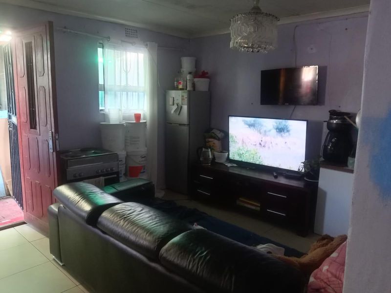 A living room area featuring tiled flooring and a ceiling light fixture, currently showing signs of wear including wall cracks and peeling paint.