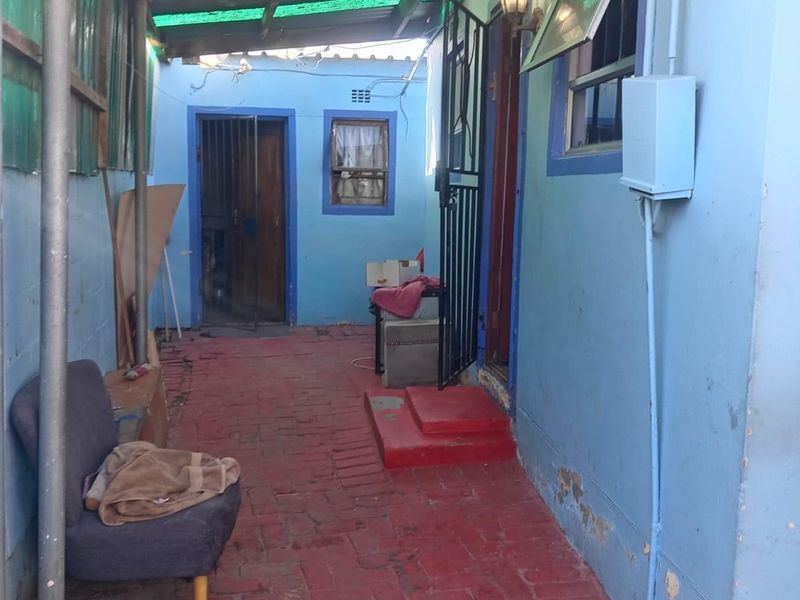 A covered outdoor patio area featuring brick paving, a corrugated roof, and security access points, showing signs of wear and requiring maintenance.