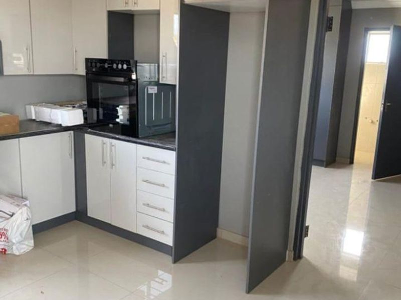 Modern kitchen featuring two-tone cabinetry, built-in oven, and polished floor tiles, offering a clean and functional space.