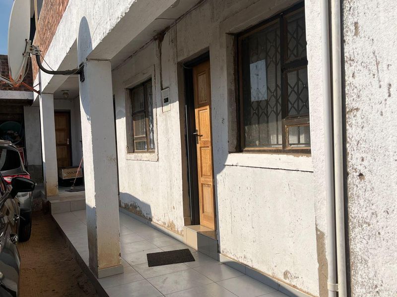 A side exterior view of the property featuring a tiled walkway, security gates, and weathered exterior walls showing signs of wear.