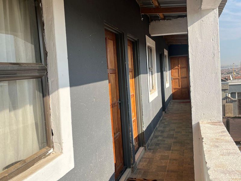 An exterior balcony featuring tiled flooring, timber doors, and an exposed roof structure, offering access to multiple rooms along the building facade.