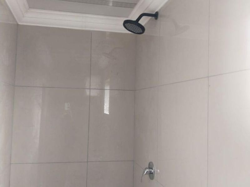 A clean, modern shower enclosure featuring neutral wall tiles, a contemporary black shower head, and a chrome mixer tap.