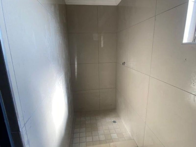 A compact shower enclosure featuring neutral wall and floor tiling, currently awaiting final plumbing fixtures and shower head installation.