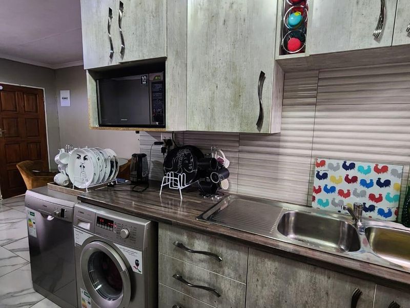 A functional kitchen featuring modern textured cabinetry, a stainless steel sink, built-in microwave, and tiled flooring with a contemporary backsplash.