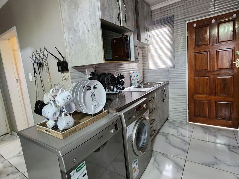 Compact kitchen featuring modern marble-look floor tiles, built-in cabinetry, integrated dishwasher, and a stainless steel sink with a tiled backsplash.