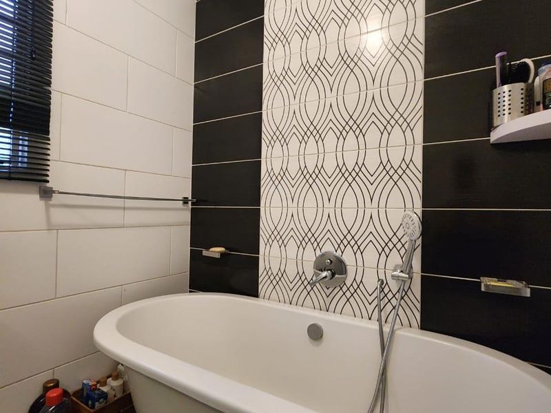 Modern bathroom featuring a freestanding bathtub with a wall-mounted mixer and handheld shower, accented by a striking black and white decorative tiled feature wall.