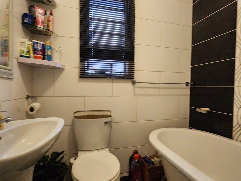A compact bathroom featuring a pedestal basin, toilet, and a classic freestanding bathtub with contrasting black and white wall tiling.