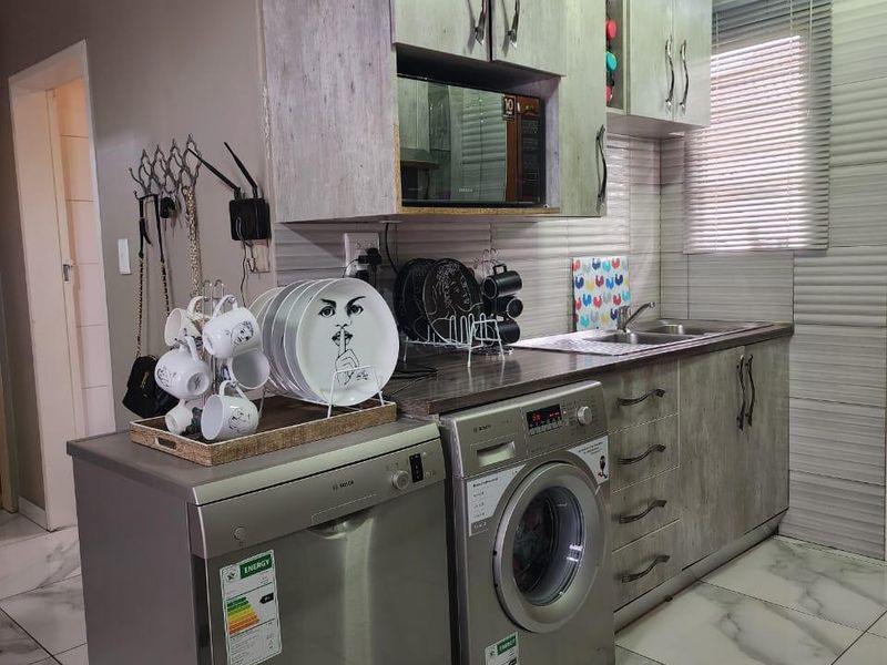 A compact kitchen featuring modern grey wood-look cabinetry, marble-effect floor tiles, integrated microwave, and stainless steel sink with venetian blinds.