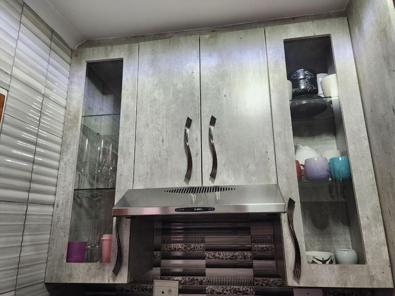 A kitchen wall section featuring built-in cabinetry with glass display panels and a stainless steel extractor fan above a tiled backsplash.
