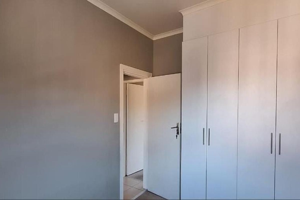 A clean, neutral bedroom featuring ample built-in cupboard storage and classic cornice detailing.