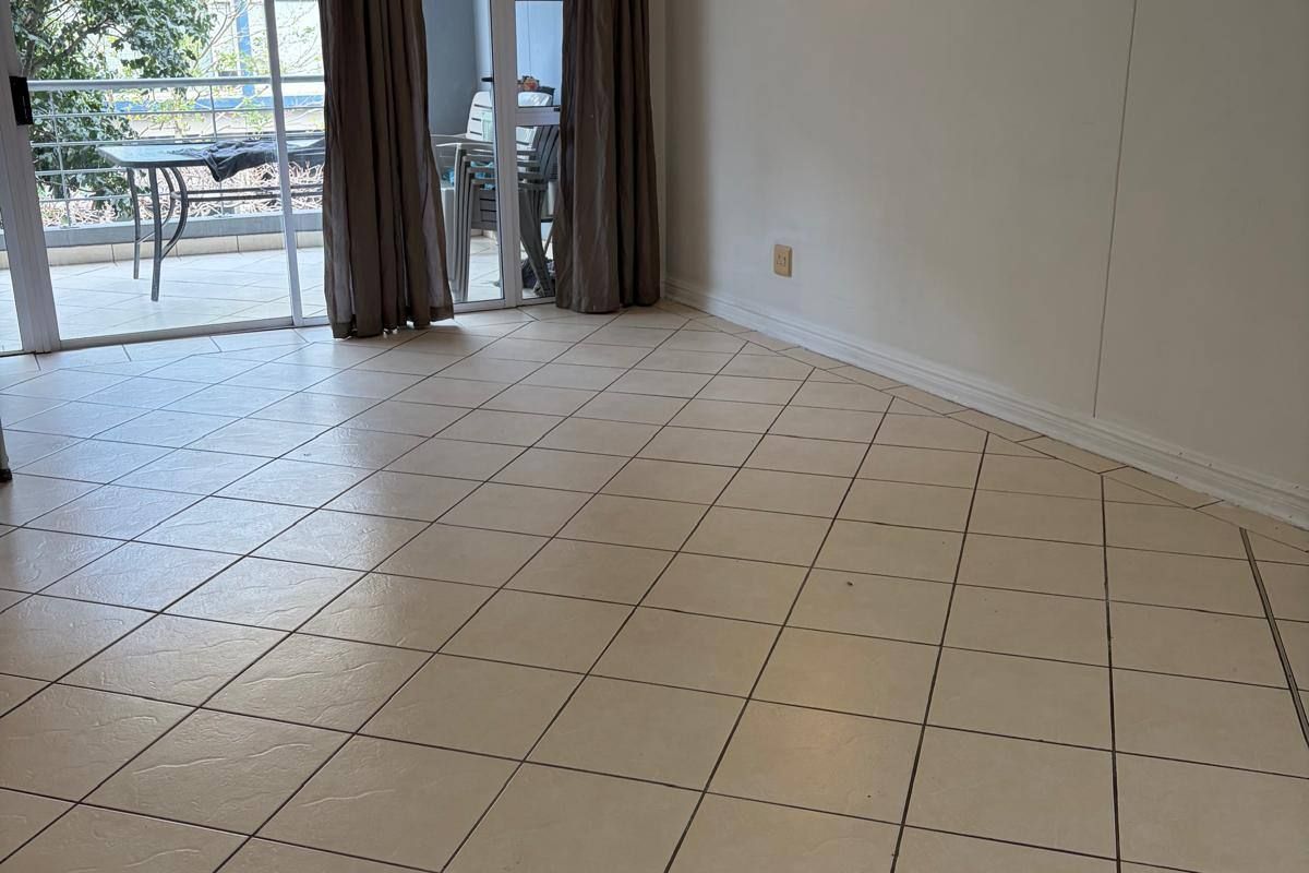 An empty, tiled living room featuring a wall-mounted air conditioning unit and sliding glass doors that open onto a balcony.