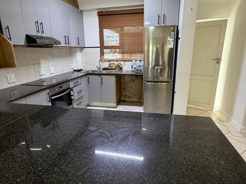 Modern kitchen featuring granite countertops, built-in oven, hob, extractor fan, and ample cabinetry, with a functional layout and tiled flooring.