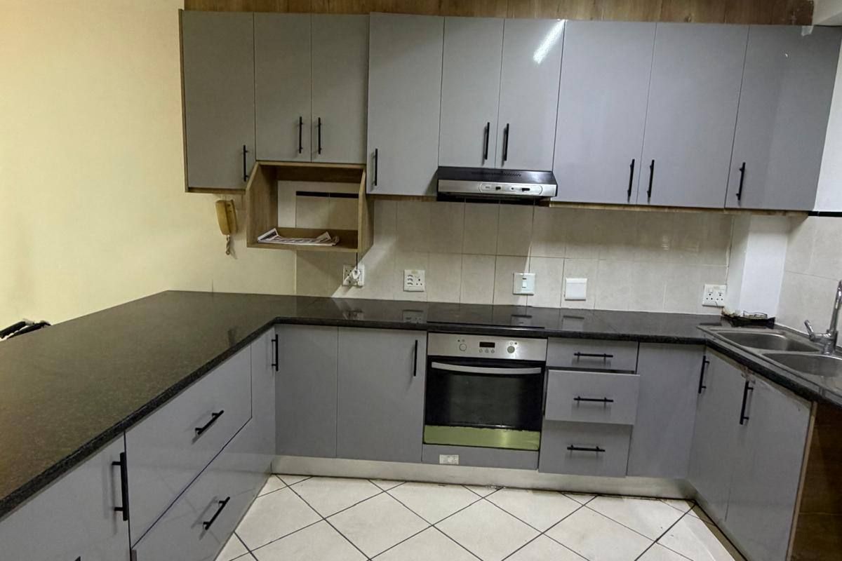 A functional kitchen featuring grey cabinetry, granite countertops, a built-in oven, and an extractor fan, finished with tiled flooring.