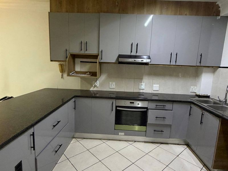 A functional kitchen featuring grey cabinetry, granite countertops, a built-in oven, and an extractor fan, finished with tiled flooring.