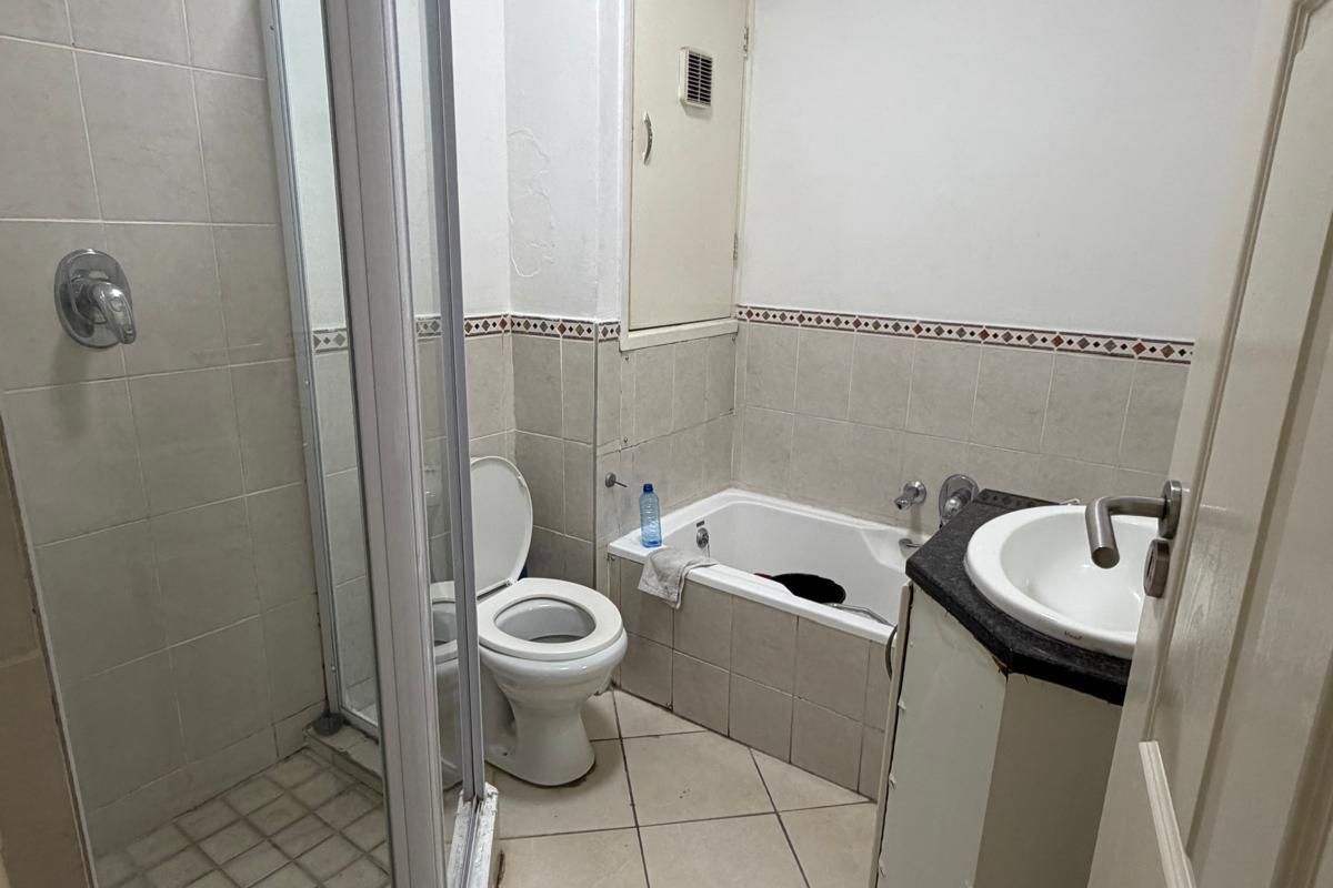 A functional bathroom featuring a shower enclosure, bathtub, toilet, and vanity basin with tiled finishes, requiring some cosmetic updates to the cabinetry and walls.