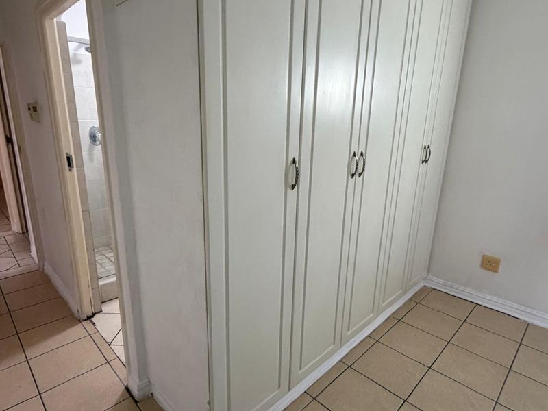 A bedroom area featuring built-in cupboards, tiled flooring, and direct access to an en-suite bathroom.
