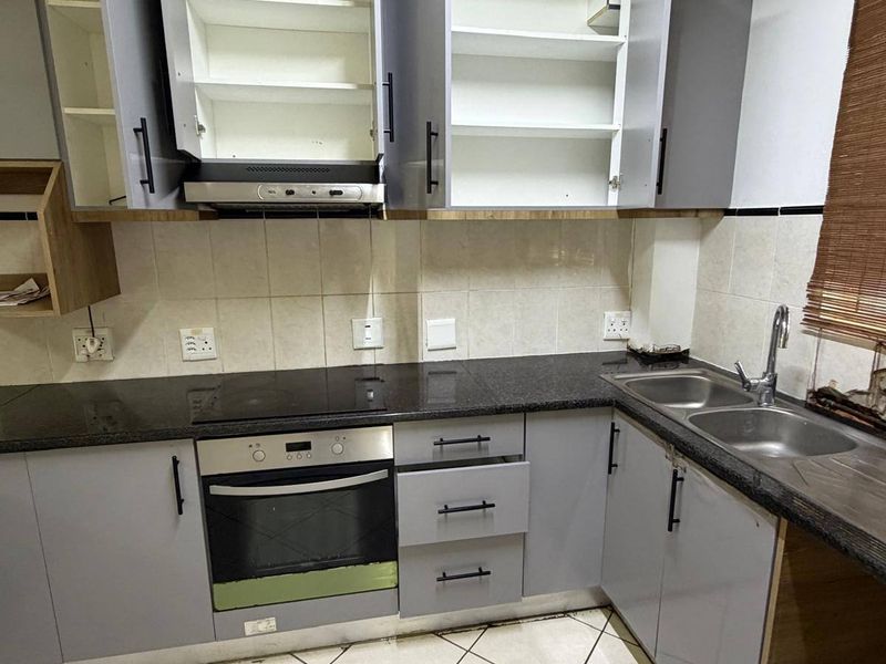 A functional kitchen featuring grey cabinetry, granite countertops, a built-in oven and hob, and tiled flooring. The space is currently vacant.