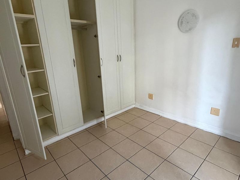 An empty bedroom featuring tiled flooring and built-in cupboards with shelving and hanging space.