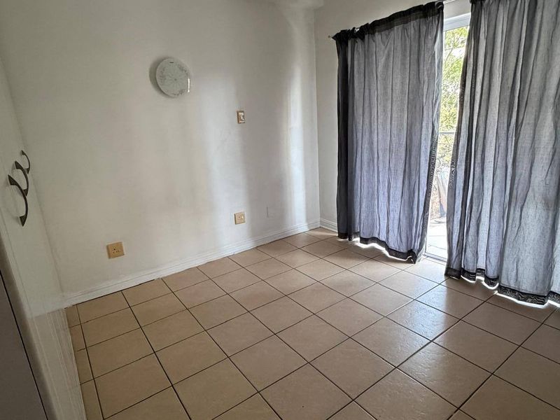 An empty bedroom featuring neutral tiled flooring and a sliding glass door providing access to an outdoor area.