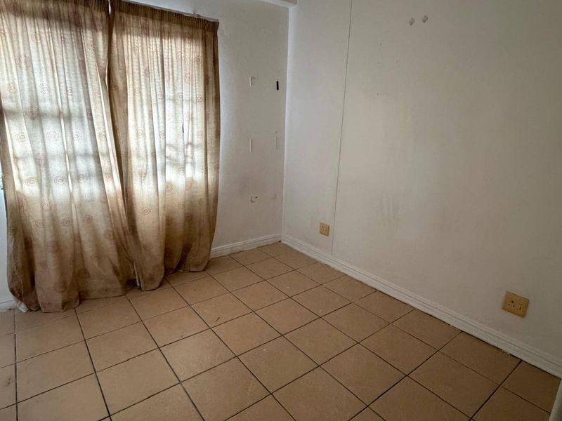 An empty bedroom featuring tiled flooring and neutral walls, ready for renovation or staging to enhance its appeal.