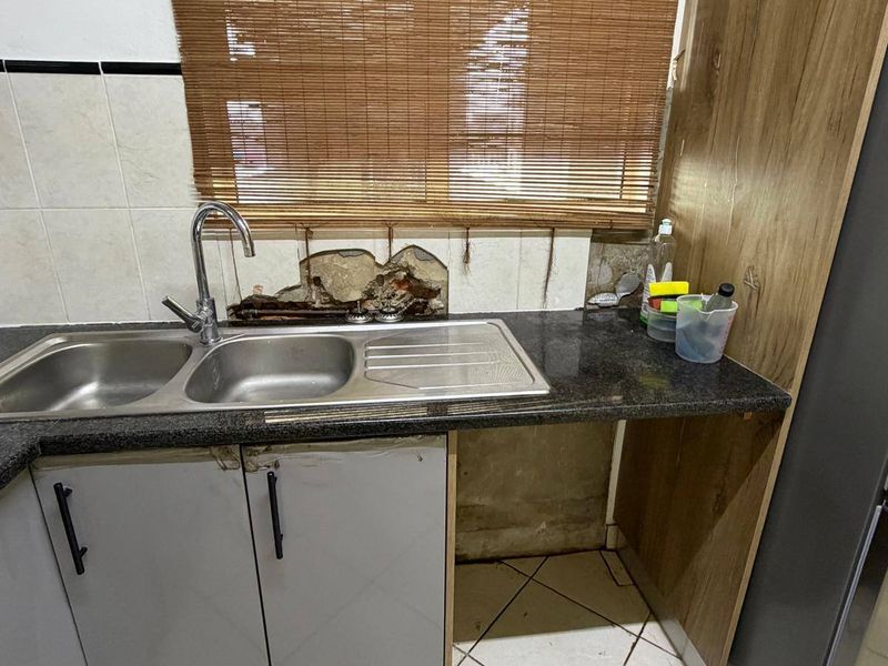 Kitchen area featuring a double bowl sink, granite countertops, and tiled flooring, currently showing significant damage to the wall plaster and cabinetry finishes.