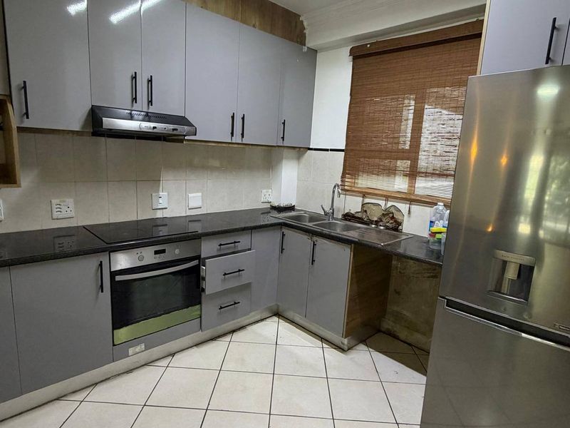 A functional kitchen featuring grey cabinetry, granite countertops, built-in oven, extractor fan, and tiled flooring with a neutral backsplash.