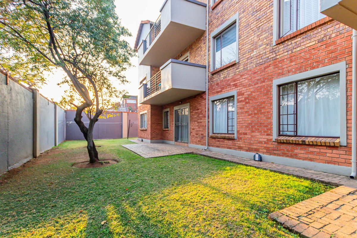 Rear view of the apartment building featuring a face brick facade, private balconies, a paved patio area, and a shared garden space.