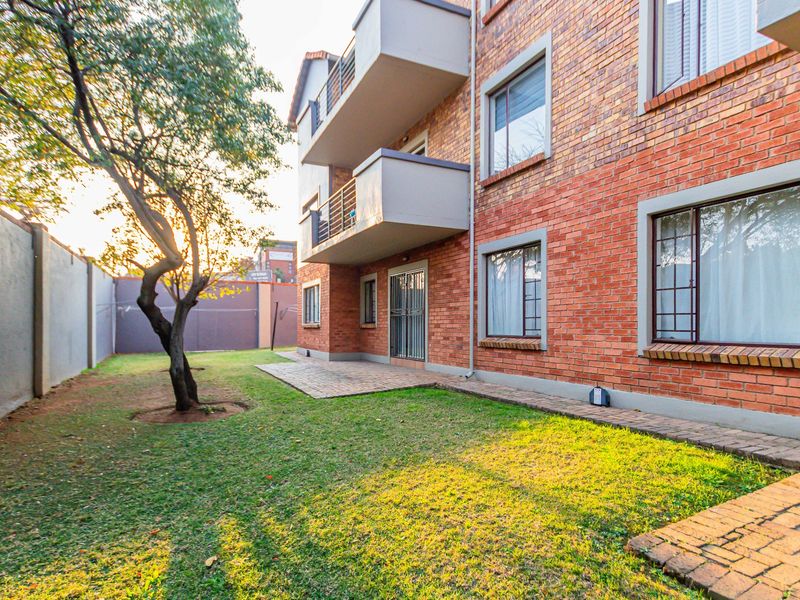 Rear view of the apartment building featuring a face brick facade, private balconies, a paved patio area, and a shared garden space.