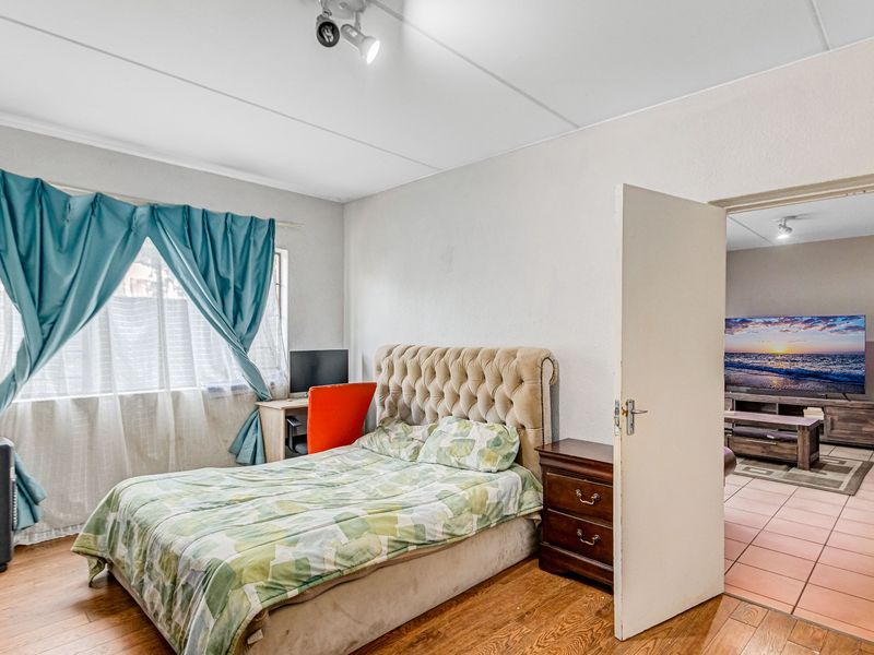 A bedroom featuring laminate flooring and a ceiling-mounted spotlight, with an open doorway leading to an adjacent living area.