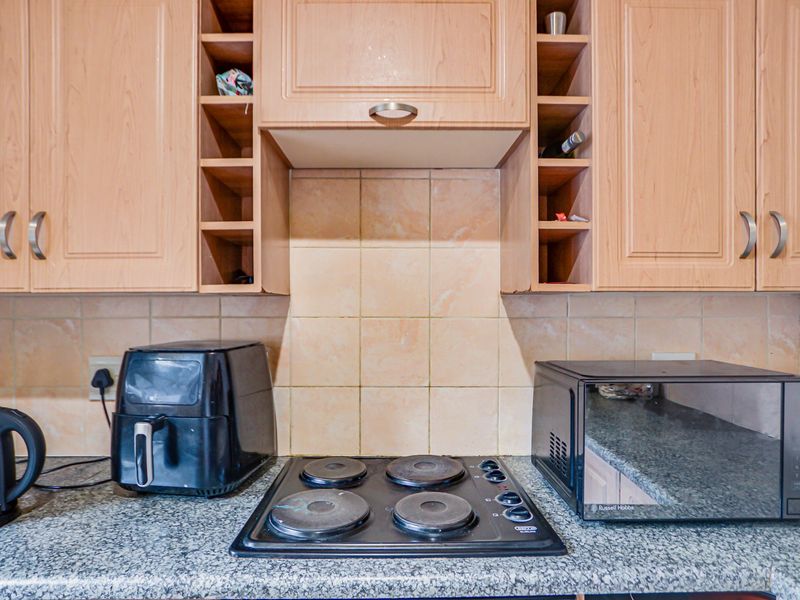 A functional kitchen area featuring light wood-toned cabinetry, a tiled splashback, and a four-plate electric hob set into a durable countertop.