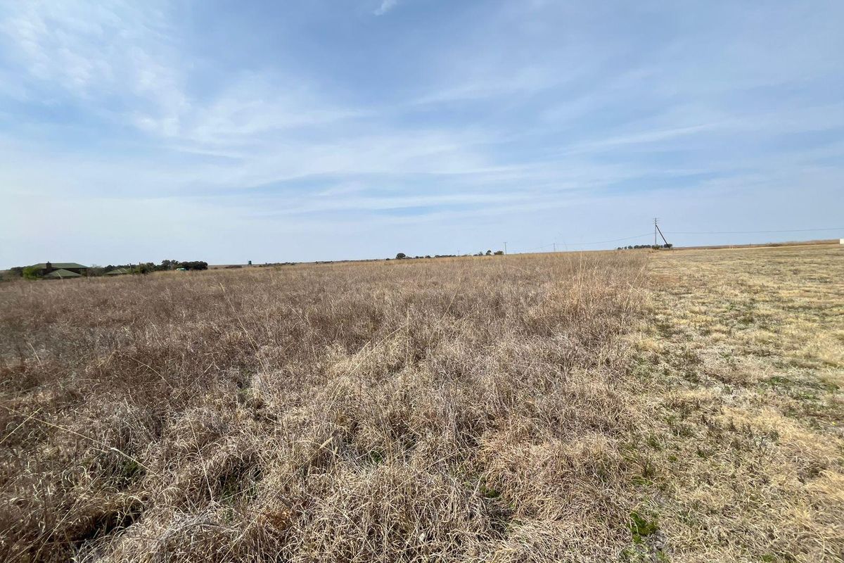 Expansive open farmland landscape featuring dry grass fields under a clear blue sky.