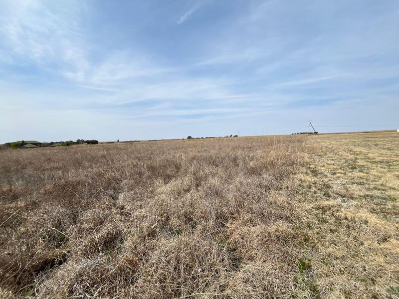 Expansive open farmland landscape featuring dry grass fields under a clear blue sky.